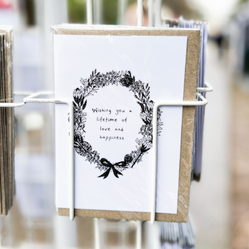 A black and white illustrated greeting card reading "Wishing you a lifetime of love and happiness" displayed on a card rack.